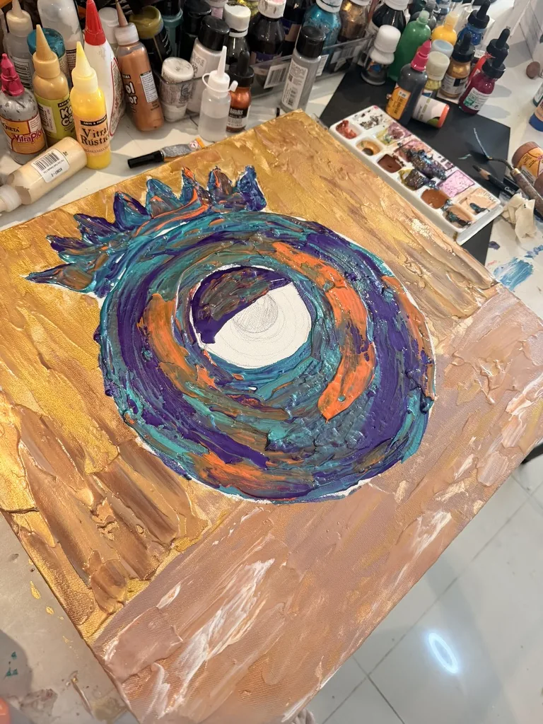 El mismo cuadro en proceso: capas gruesas de pintura morada, turquesa y naranja sobre fondo dorado; el ojo de Ojai aún está en blanco.