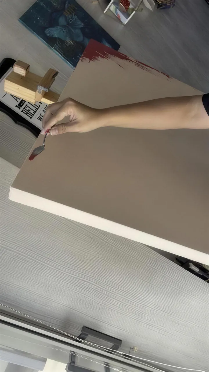 La mano de Stephie pone pintura roja con una espátula en el borde del lienzo.