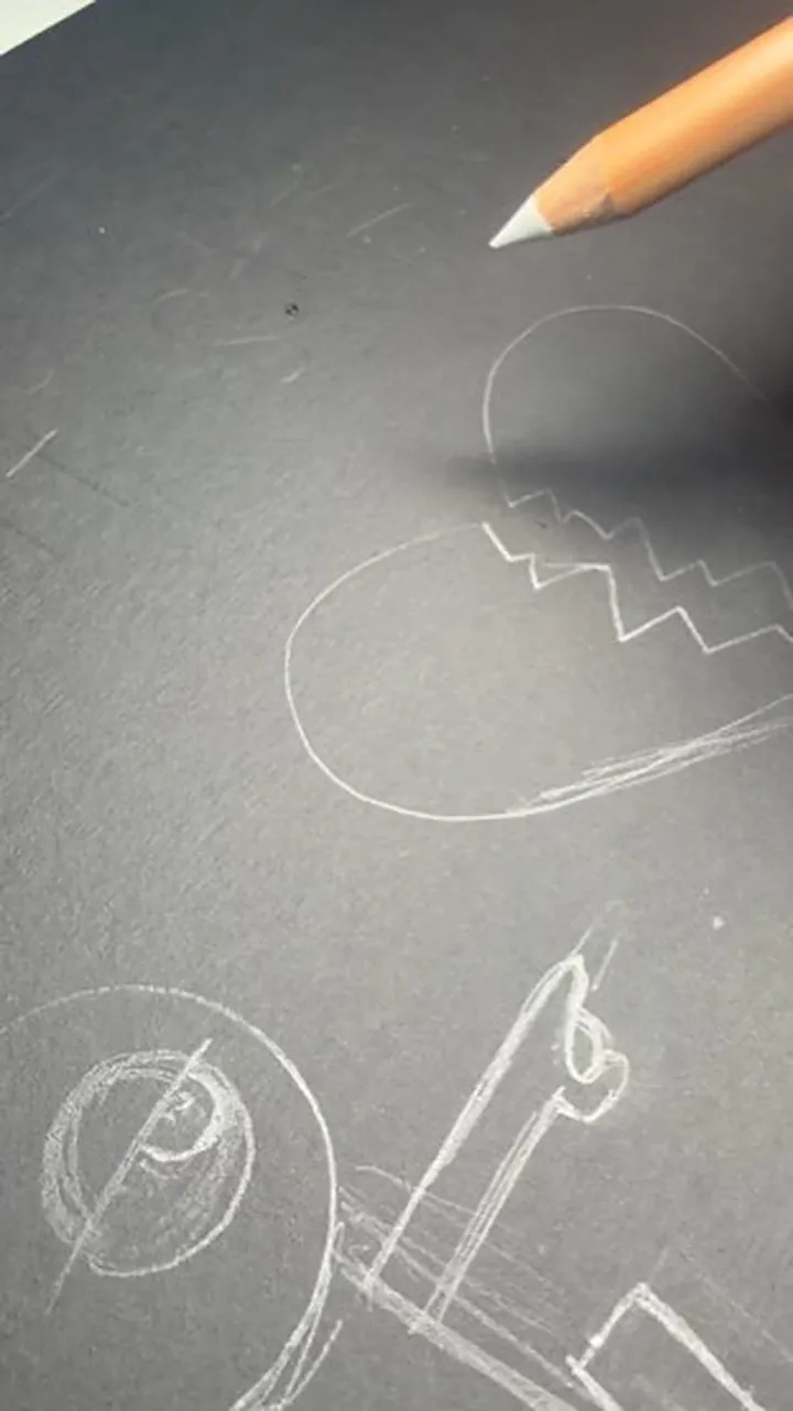 Una mano dibuja con lápiz blanco sobre papel negro las primeras líneas de un corazón partido.
