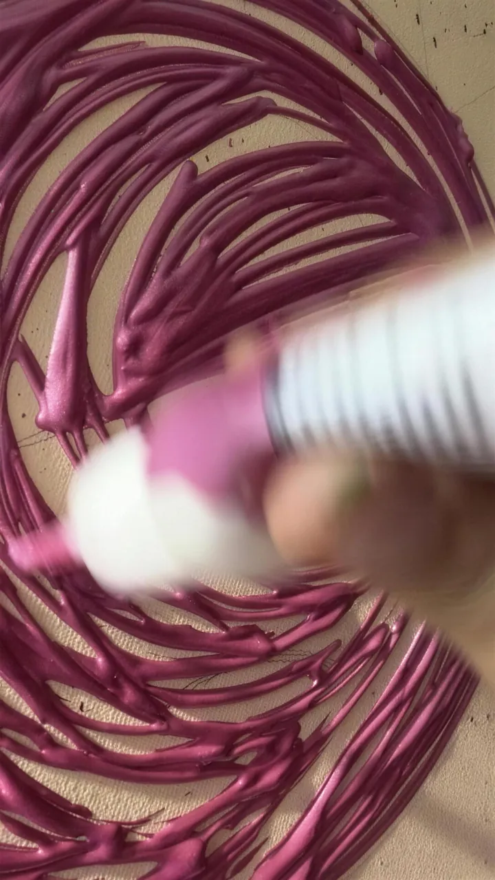 Pintura rosada muy gruesa sale de una botella y forma espirales con relieve.